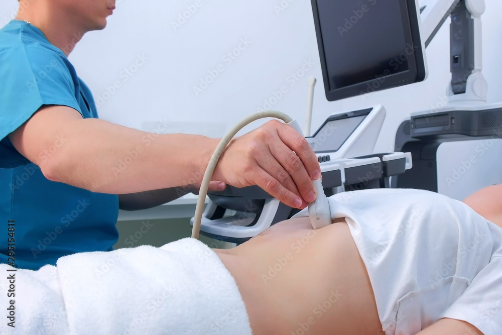 Wall mural Man doctor making abdominal ultrasound to diagnosis stomach of woman in clinic. He runs ultrasound sensor over patient's tummy and looks at image on screen. Diagnosis of internal organs.