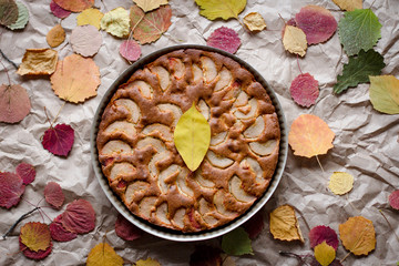 Fototapeta premium autumn browned fruit cake decorated with bright fallen leaves, top view