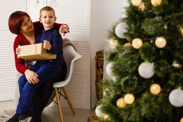 In the living room with a fireplace and a Christmas tree, mother and her son are packing a present for Christmas
