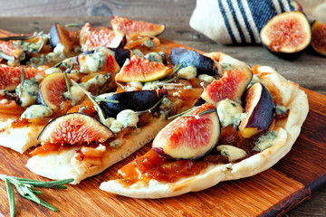 Autumn flat bread pizza with figs, caramelized onions, blue cheese and rosemary. Close up side view on a wood serving board.