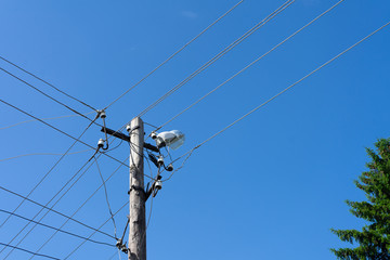 Old wooden electric pole with a lamp and many cables that run in different directions, cloud sky.