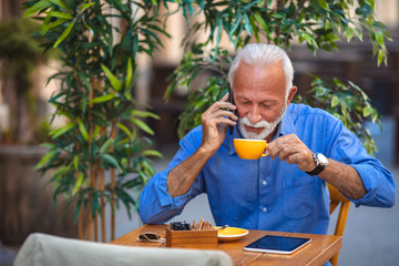 Portrait of a bearded senior man drinking coffee in a cafe. Senior man using smart phone in cafe. Senior Businessman Using Smart Phone outdoors. Portrait of happy senior man sitting in cafe