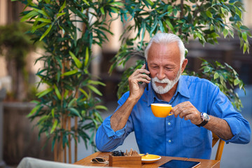 Portrait of a bearded senior man drinking coffee in a cafe. Senior man using smart phone in cafe. Senior Businessman Using Smart Phone outdoors. Portrait of happy senior man sitting in cafe