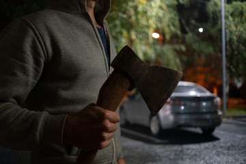 A man with an ax is about to damage the car at night.