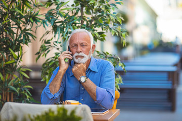 Portrait of senior man sitting in cafe and talking with smarphone. Portrait of senior man working with cellphone in outdoor cafe lounge. Man working as freelancer
