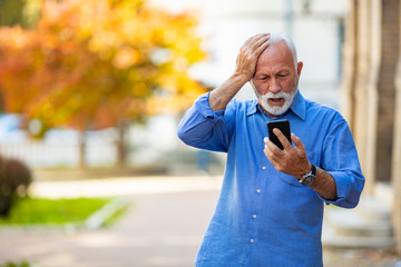 Handsome senior man using smartphone sending message stressed with hand on head, shocked with shame and surprise face, angry and frustrated. Fear and upset for mistake.