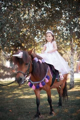 Foto op Canvas Little girl in a beautiful dress of pink color in the park with a brown pony. © Eugenia Sh