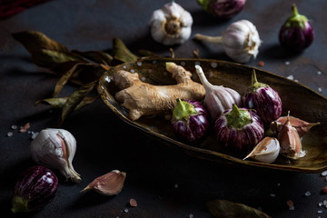 Mini Eggplants, ginger, garlic in handmade ceramic plate, crystalline pink salt on concrete background 