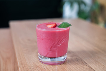 Fresh bio strawberry smoothie close-up on a wooden table, Paris, France. Beautiful glass with a piece of fruit on the top and basil ! Blurred background.