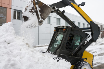 A small snowplow tractor removes snow drift from the street. Selective focus.