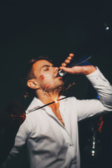 Fun celebration. Wasted handsome playboy with lipstick kisses on his cheek drinking wine from bottle.