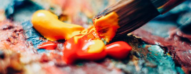 Modern fine art school. Closeup of paintbrush mixing red and yellow acrylic paint on colorful...