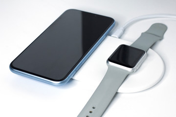 Cell mobile smartphone and smartwatch charging on a wireless charge. New devices, equipment. Modern technology concept. Still life, composition of gadgets: phone, watches, charger. Easy way to charge. - obrazy, fototapety, plakaty