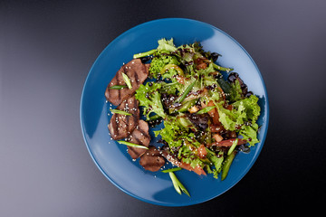 Veal salad with lettuce, apple, pear and tomato on blue plate on dark wooden background, copy space. Restaurant food, close up. Meat salad