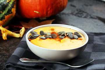 Roasted pumpkin and carrot soup with cream and pumpkin seeds on wooden background.