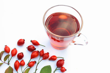 Rosehip tea surrounded by fruit and leaves on a white background