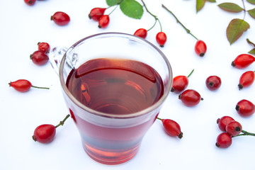 Rosehip tea surrounded by fruit and leaves on a white background