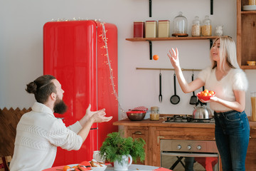 Winter holidays fun. Couple playing with mandarins in modern kitchen, lady throwing fruit to her...