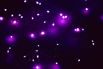 Cold white LED string lights over defocused purple glow. Dark abstract festive background.