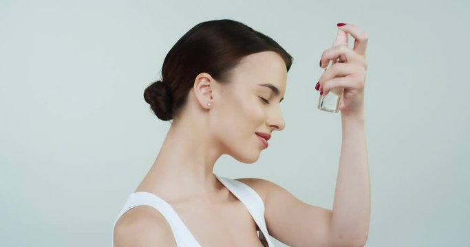 Young Caucasian attractive woman in white T-shirt taking care of her health and beauty spraying parfume on ner neck and hair. Close up.
