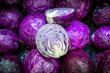 Red cabbages for sale on a market stall, with one of them cut to show the pattern of the leaves