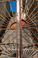 A set of ornate rusting gates partially open and leading to a set of concrete steps