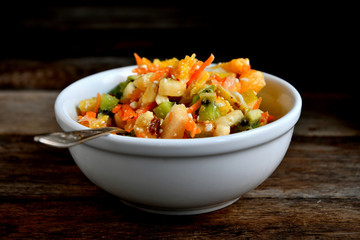 Fruit salad in a white bowl on a wooden table.