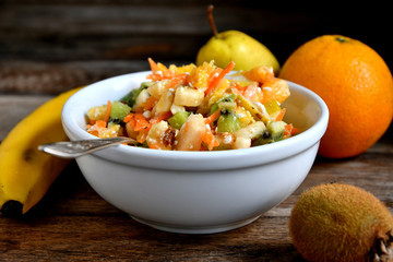 Fruit salad in a white bowl on a wooden table.
