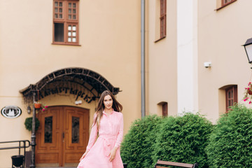 Fototapeta premium A young, beautiful girl in a pink dress walks around the city. Photo close - up and General plan. Girl sitting on a bench.