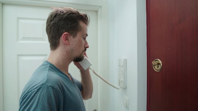 Man answers the intercom and open the door 4K. Medium side shot of male person in focus walk into the frame picking the intercom.