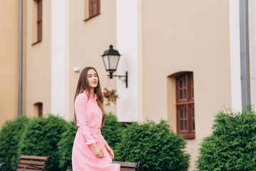 A young, beautiful girl in a pink dress walks around the city. Photo close - up and General plan. Girl sitting on a bench.