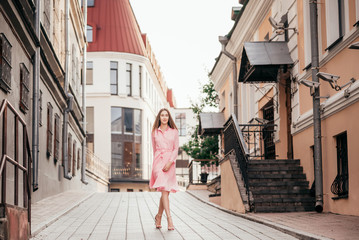 A young, beautiful girl in a pink dress walks through the beautiful streets in the city. Very beautiful portraits of a girl in the city.