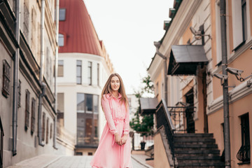 Naklejka premium A young, beautiful girl in a pink dress walks through the beautiful streets in the city. Very beautiful portraits of a girl in the city.