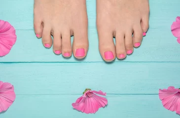 Foto op Plexiglas hete roze pedicure. bovenaanzicht van benen met pedicure. been tegen de achtergrond van blauwe borden rond roze bloemen. blauwe houten achtergrond © FytyaKarman