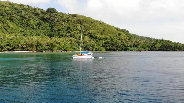 aerial pan around a catamaran yacht anchored off a tropical island in clear blue water