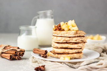Stack of delicious sweet and spicy apple pancakes with fried caramelized apples and spices (anise and cinnamon) on a white plate. Autumn breakfast. 