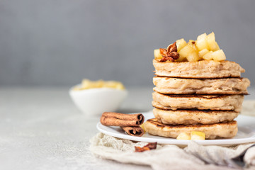 Stack of delicious sweet and spicy apple pancakes with fried caramelized apples and spices (anise and cinnamon) on a white plate. Autumn breakfast. 