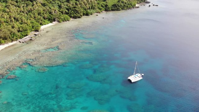 Aerial view of a catamaran yacht anchored in clear water off a tropical island with coral reef and palm trees in Vanuatu