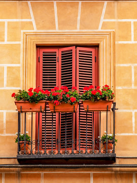 A juliet balcony with red louvre doors and small red flowers in window planters