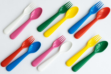 Colored bright plastic dishes beautifully laid out on a white background. Knives, forks, spoons....