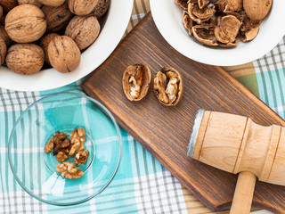 Whole walnuts, shells and kernels in a bowls around a brown wooden board with cracked nuts and wooden meat mallet. Natural unbleached Juglans regia.