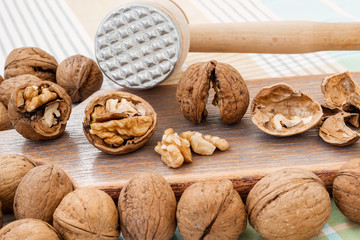 Front view of whole and cracked walnuts (Juglans regia) near wooden meat mallet on a brown wooden board. Natural unbleached nuts. Vegetarian.