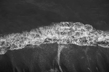 Looking down on breaking waves on beach in black and white