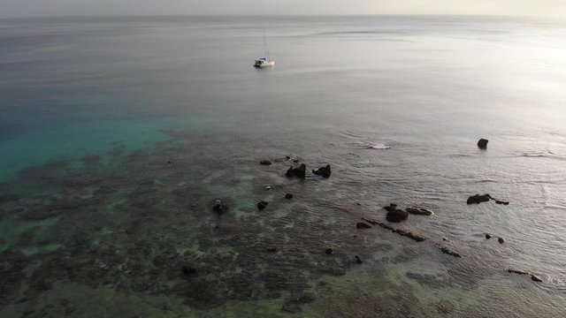 Aerial view of a catamaran yacht anchored in clear water off a tropical island with coral reef and palm trees in Vanuatu