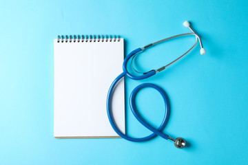 Stethoscope and notepad on a blue background, space for text