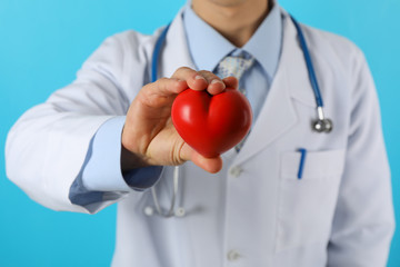 Doctor with stethoscope and heart against blue background, close up