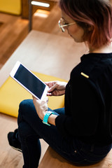 Photo of a young student working on her electronic tablet sitting in the auditorium. She wears jeans, glasses and a watch. Mobile and technology app