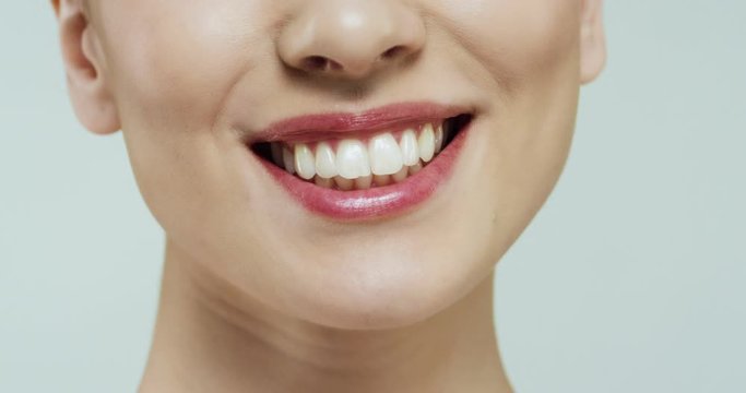 Close up of the bottom part of the female face, mouth and nose of the Caucasian woman on the white wall background while she laughing cheerfully with white teeth.