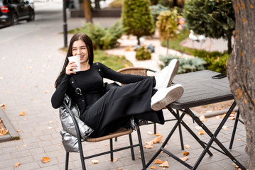 girl in black clothes and white sneakers drinking coffee and talking on the phone