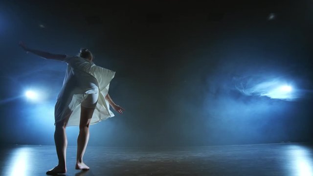 Modern ballet dancing woman barefoot doing spins and pirouettes and dance steps standing on stage in smoke in slow motion. Performance on stage
